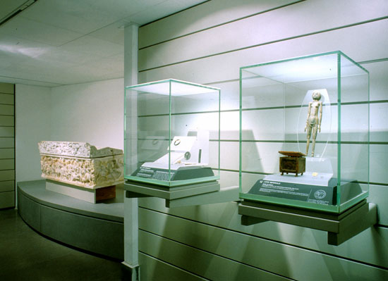 Figura 10 - Alcune vetrine della sala del lusso con corredi funerari di età romana; a sinistra, il sarcofago entro il quale fu rinvenuta la mummia della bambina di via di Grottarossa (Roma)